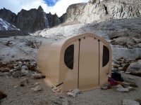 A small beige tent is set up among rocky mountains.