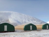 Three green and beige shelters stand in a snowy landscape