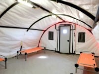 The inside of a white tent has two orange cots and a door with a small window