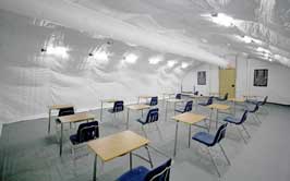 A classroom with several desks and chairs inside a white tent