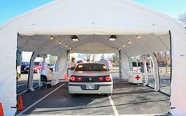 A car is getting tested by people in protective suits inside a large white fabric tent