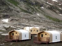 Three small beige cabins are situated in a rocky mountainous area