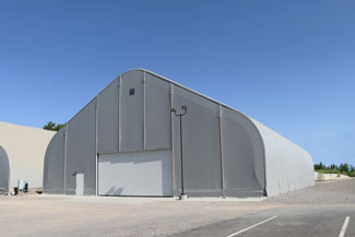 A large, grey fabric structure warehouse under a clear blue sky
