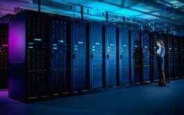 A woman works on a laptop in a dark, neon-colored server room