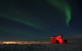 A red tent is lit up under the northern lights on a snowy landscape