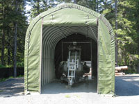 A boat is stored inside a green fabric shelter in a forested area