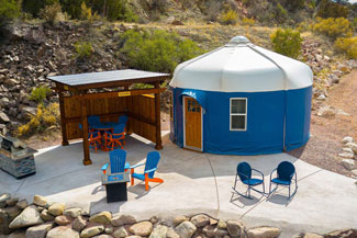 A blue yurt with a patio set up in a rocky area