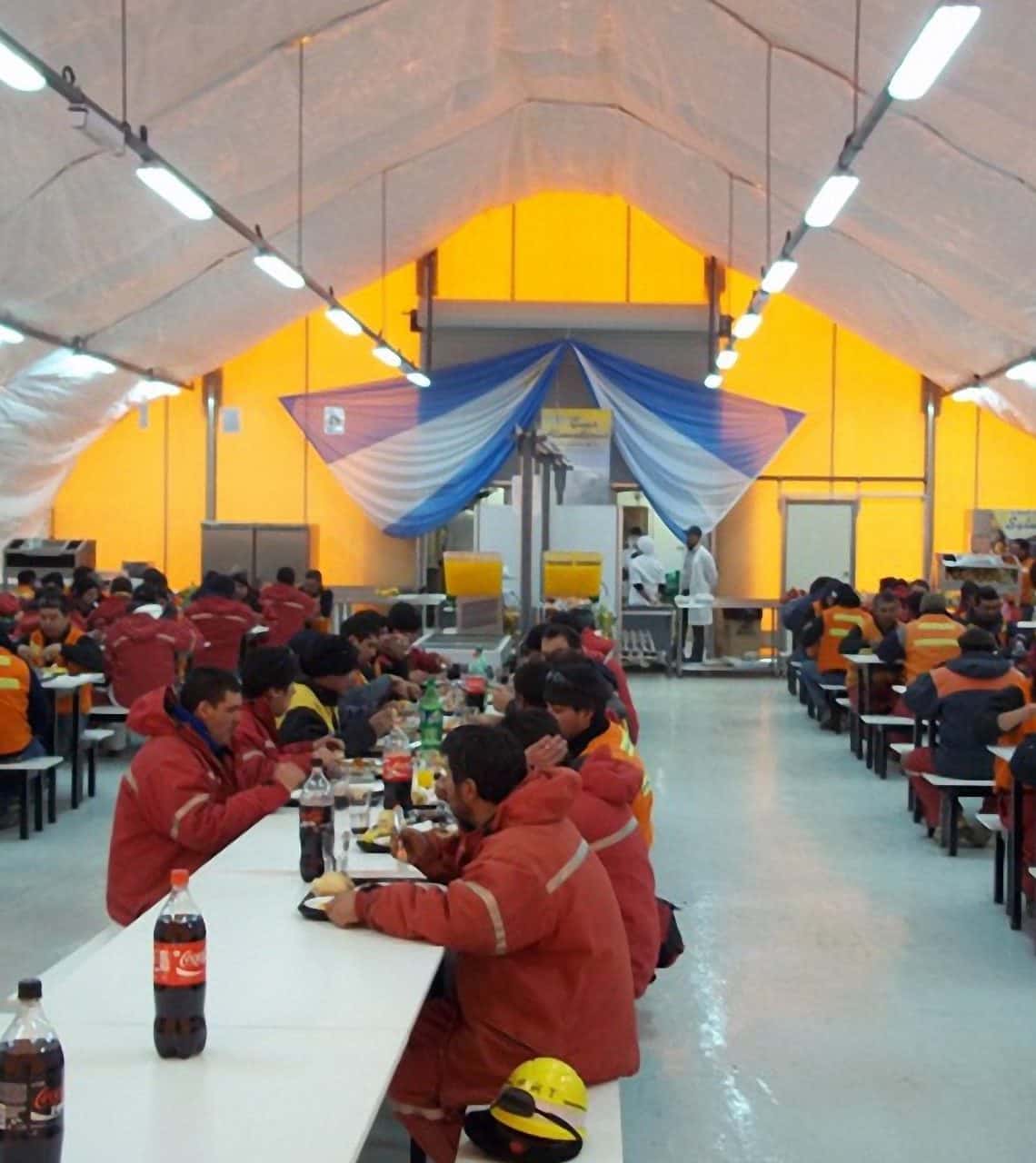 The interior of a dining hall at a remote mining camp in South America features a DAGB Series™ fabric building from Alaska Structures®, seamlessly connected to kitchen containers for efficient meal preparation and dining.