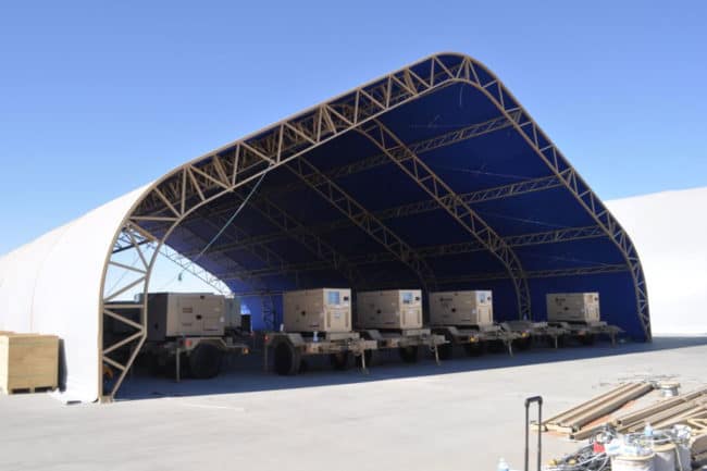 alaska-structures-industrial-warehouse-and-storage-building-8 A large open-ended warehouse, featuring a tan powder-coated frame DAGB Series™ fabric building from Alaska Structures®, protects trailer-mounted generators from sun exposure and adverse weather conditions.
