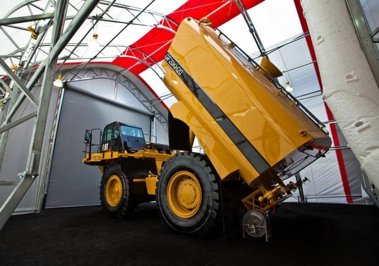 A large yellow construction vehicle is inside a tent with red and white stripes