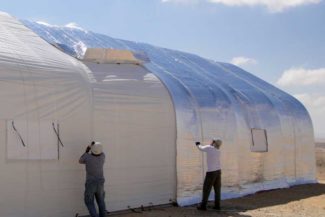 Two men working on installing a large white tent in a desert area