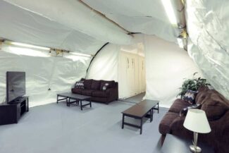 Interior of a 20' x 30' SQ Series™ workforce housing dormitory featuring a recreation area, soft-wall partition system for private sleeping quarters, HVAC and ventilation equipment, and a lighting and electrical package. Designed to improve occupant comfort and morale, the structure provides comfortable workforce accommodations for personnel operating in remote locations and extreme environments.