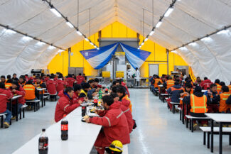 Construction workers dining inside a large lunch tent connected to containerized kitchen facilities at a remote mine site.